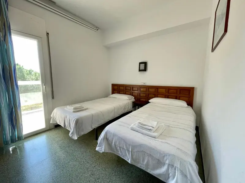 Une chambre lumineuse avec deux lits simples et une porte-fenêtre.