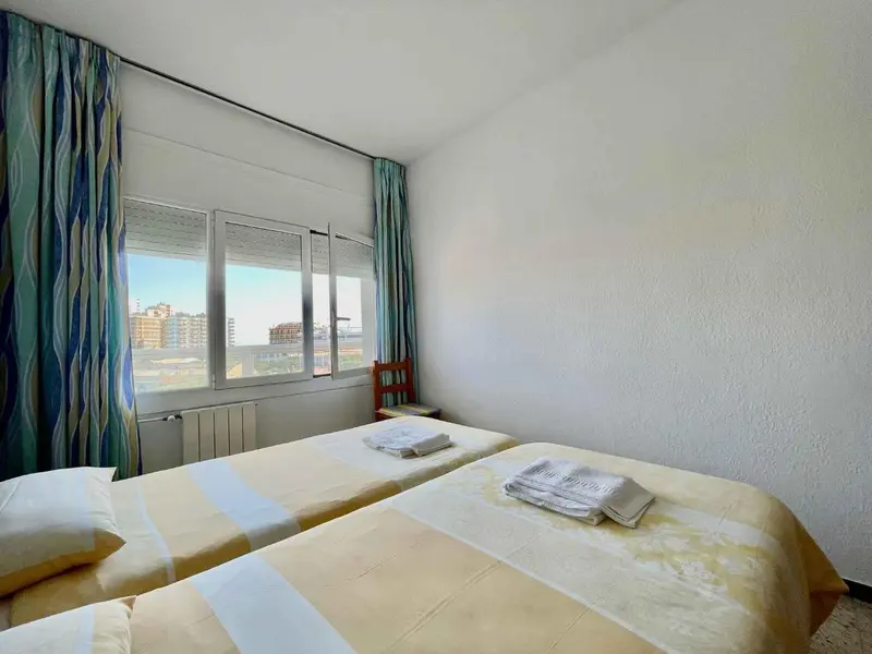 Chambre lumineuse avec deux lits simples et vue sur la ville.