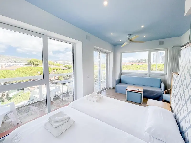 Une chambre lumineuse avec un lit et un canapé, donnant sur une vue urbaine et la mer.