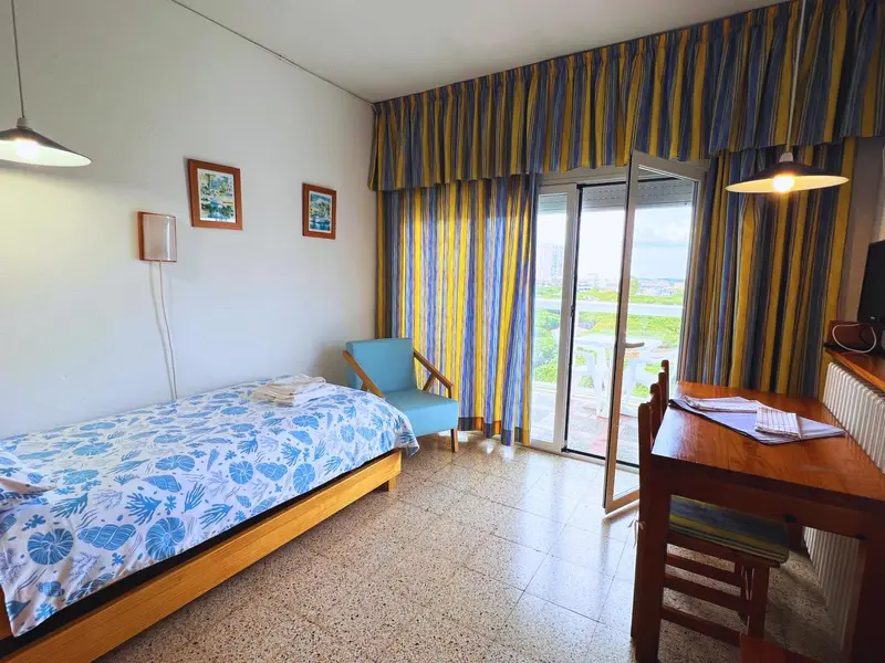 Une chambre lumineuse avec un lit recouvert d'un couvre-lit bleu et une vue sur un paysage verdoyant.