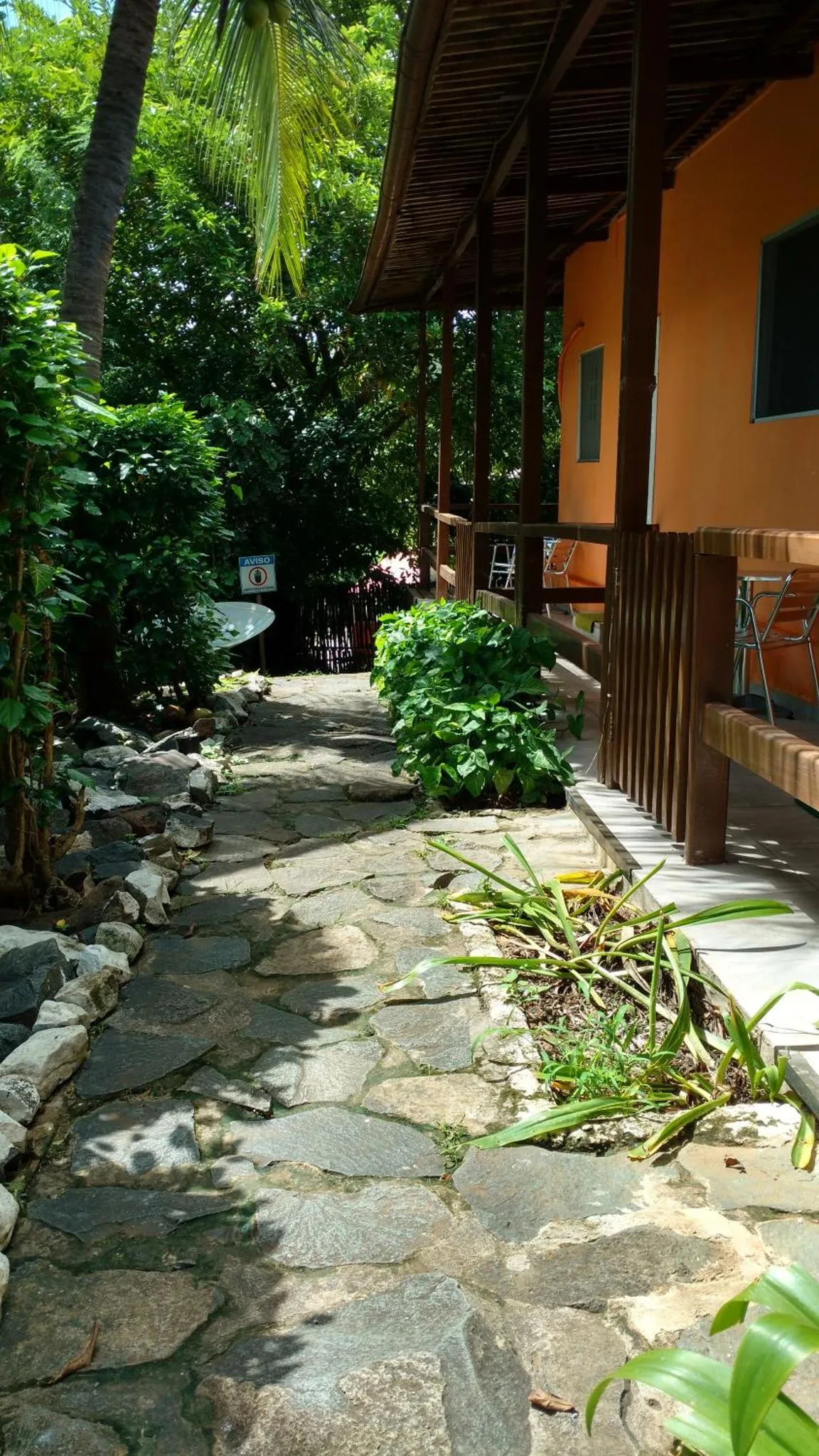 Un chemin pavé mène à une terrasse ombragée devant un bâtiment orange.