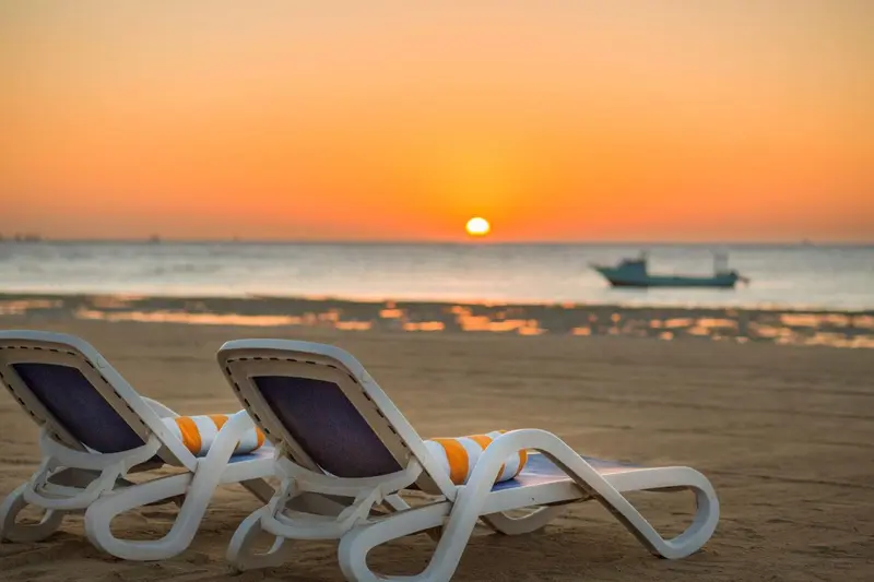 Transats sur une plage de sable au coucher du soleil.