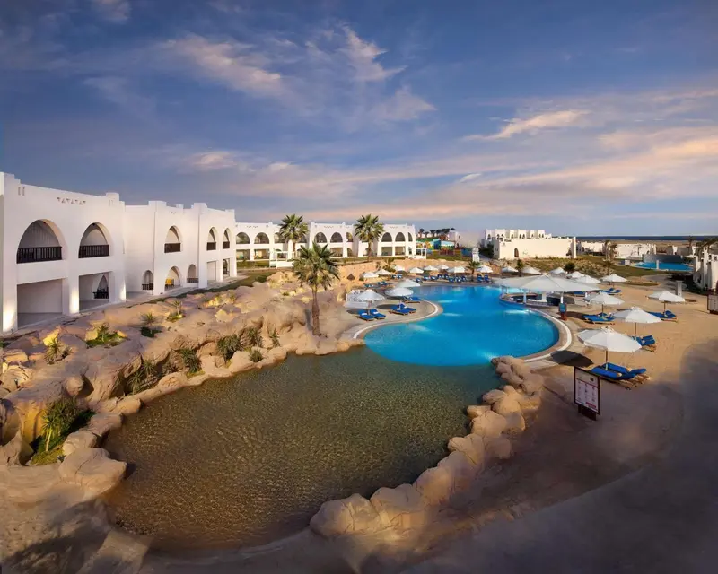 Vue aérienne d'un complexe hôtelier avec piscine et végétation luxuriante au crépuscule.