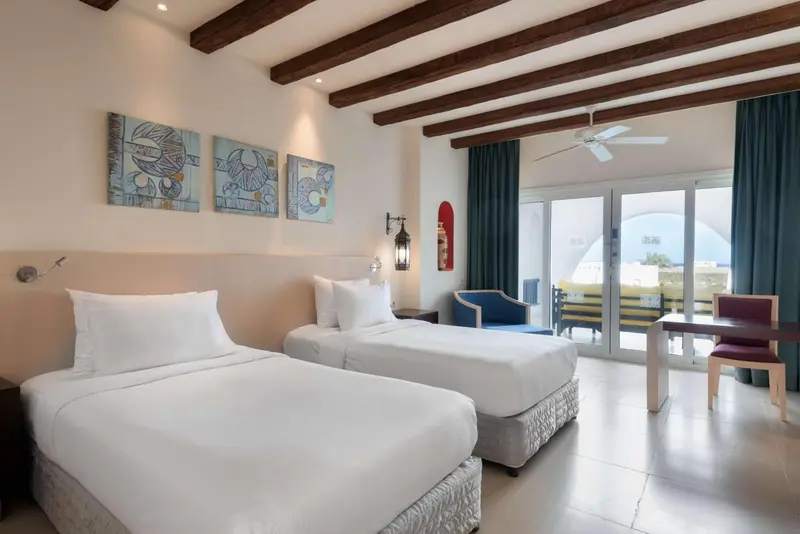 Chambre lumineuse avec deux lits simples et vue sur une terrasse.