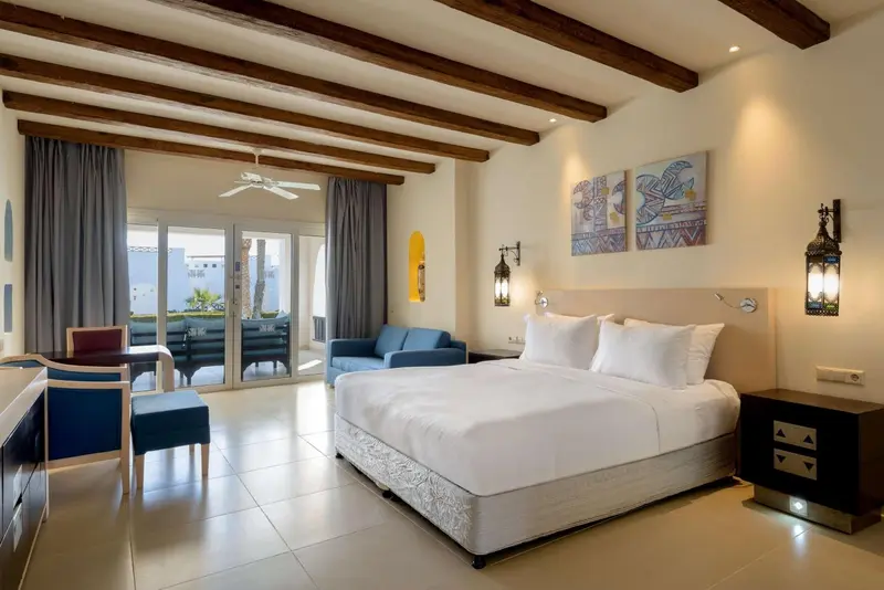 Une chambre lumineuse avec un grand lit et un coin salon donnant sur une terrasse.