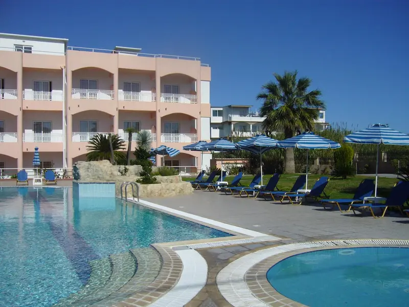 Une piscine turquoise bordée de transats bleus devant un bâtiment pastel.