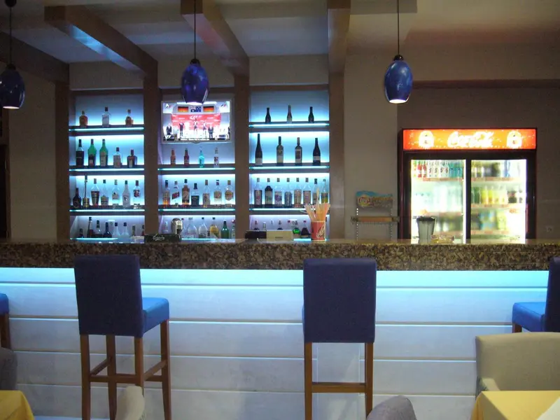 Un comptoir de bar illuminé avec des bouteilles et des tabourets.