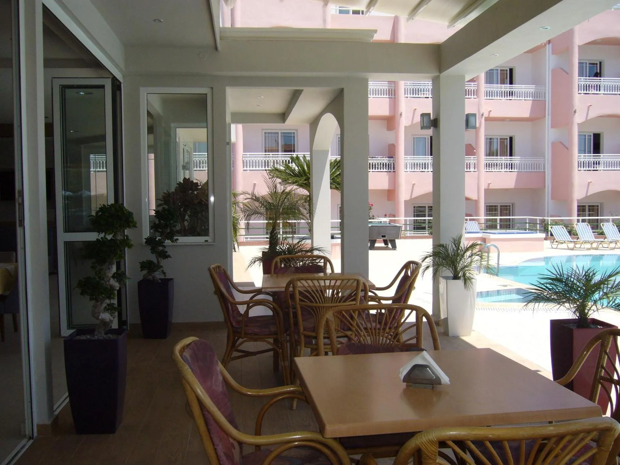 Terrasse ombragée avec tables et chaises donnant sur une piscine.