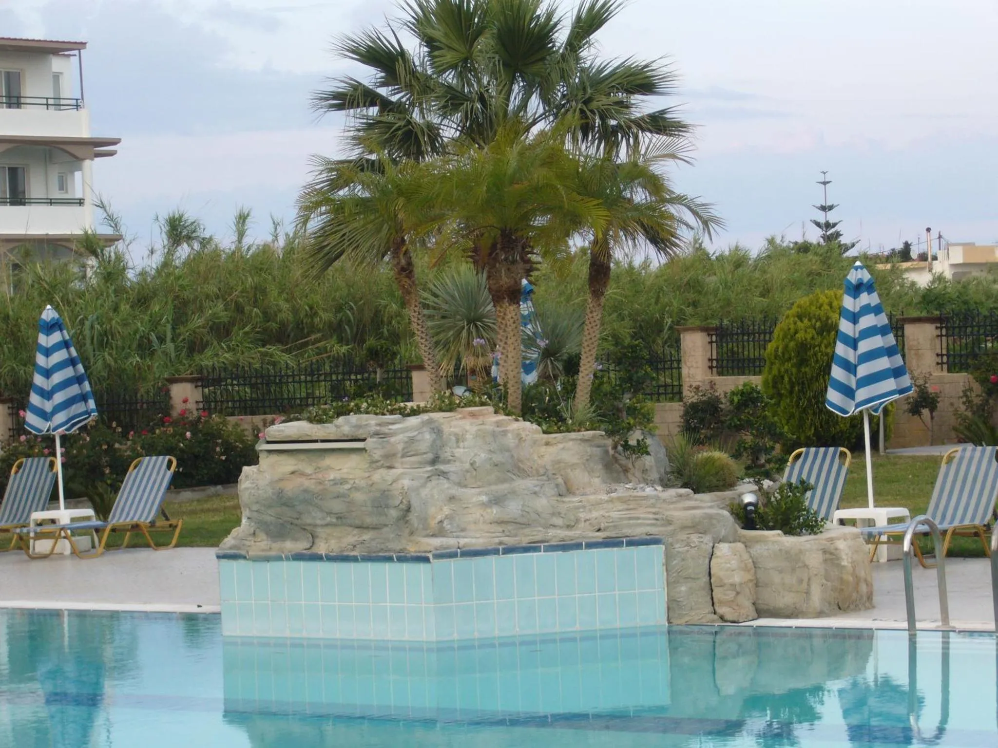 Transats bleus et blancs disposés autour d'une piscine avec un décor rocheux et des palmiers.