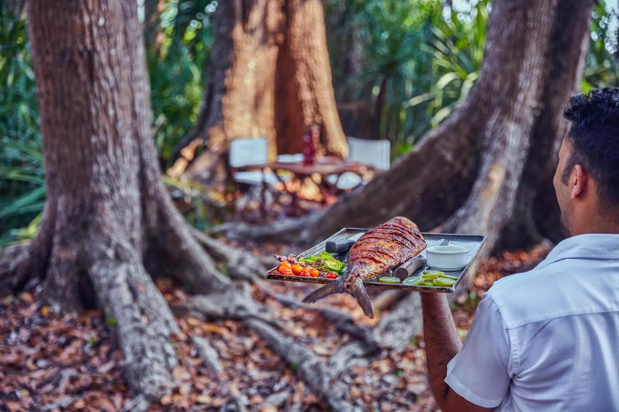 Un serveur présente un plat de poisson grillé dans un cadre tropical.