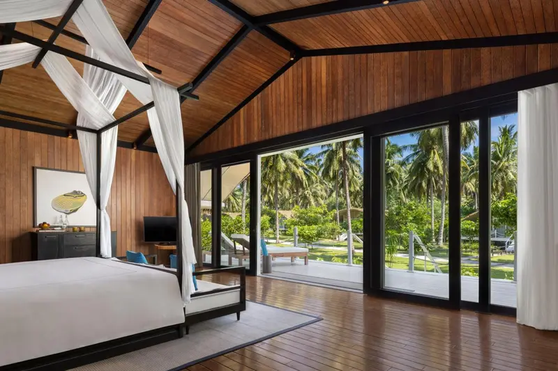 Une chambre lumineuse avec un grand lit et vue sur une végétation luxuriante.