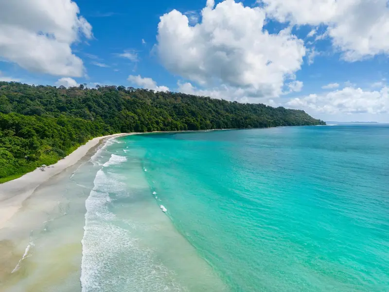 Vue aérienne d'une plage de sable blanc bordée d'une forêt tropicale luxuriante et d'une mer turquoise.