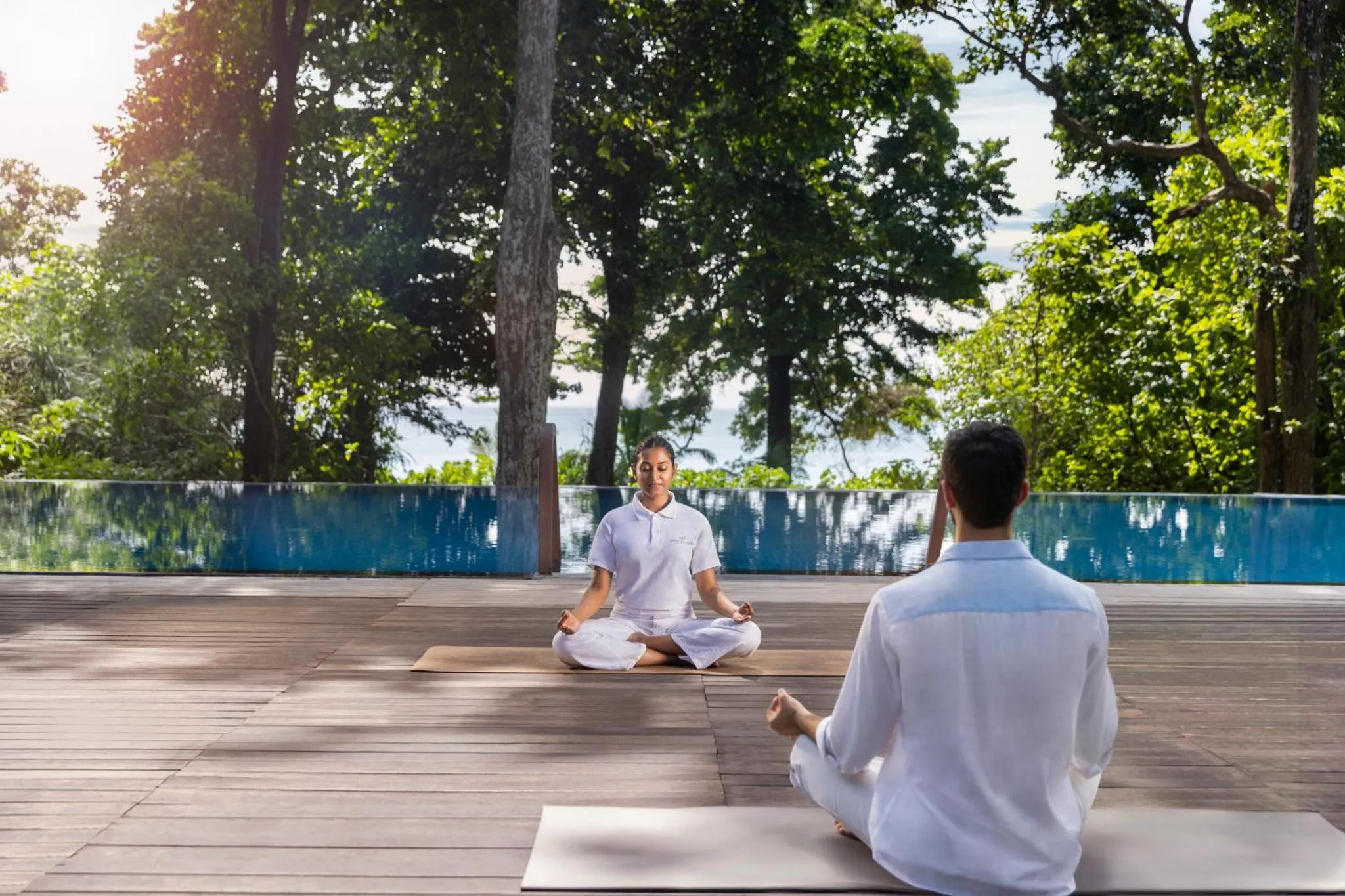 Deux personnes pratiquent le yoga sur une terrasse en bois face à la mer.
