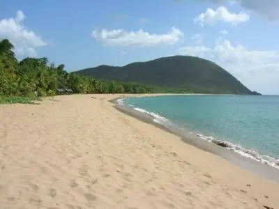 Une plage de sable fin borde une mer turquoise sous un ciel nuageux.