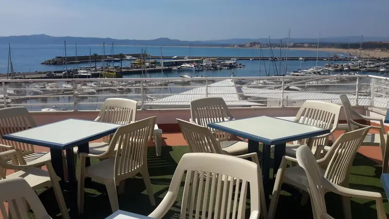 Terrasse avec tables et chaises donnant sur un port de plaisance.