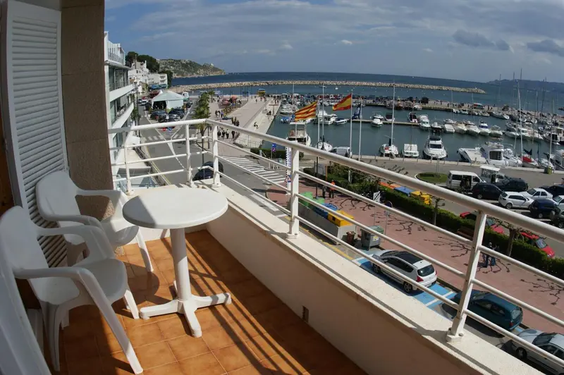 Vue d'un balcon avec mobilier en plastique donnant sur un port de plaisance ensoleillé.