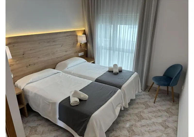 Une chambre lumineuse avec deux lits simples et une chaise.