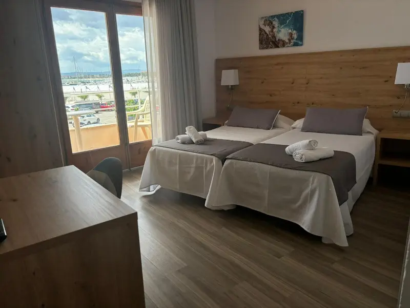 Chambre lumineuse avec lits jumeaux et vue sur un port de plaisance.