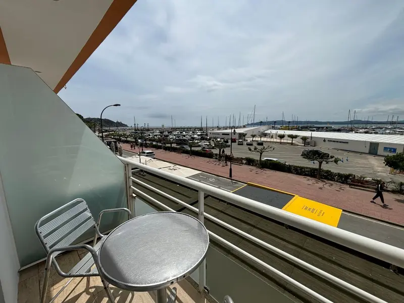 Vue d'un balcon avec mobilier donnant sur un port de plaisance et une promenade.