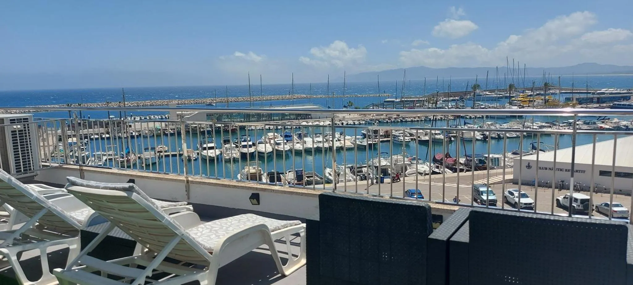 Terrasse avec transats donnant sur un port de plaisance ensoleillé.