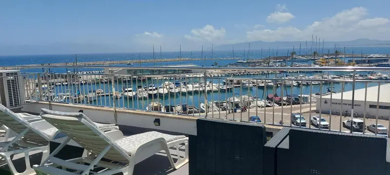 Terrasse avec transats donnant sur un port de plaisance ensoleillé.