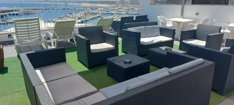 Espace de détente extérieur avec mobilier en résine tressée et vue sur un port de plaisance.