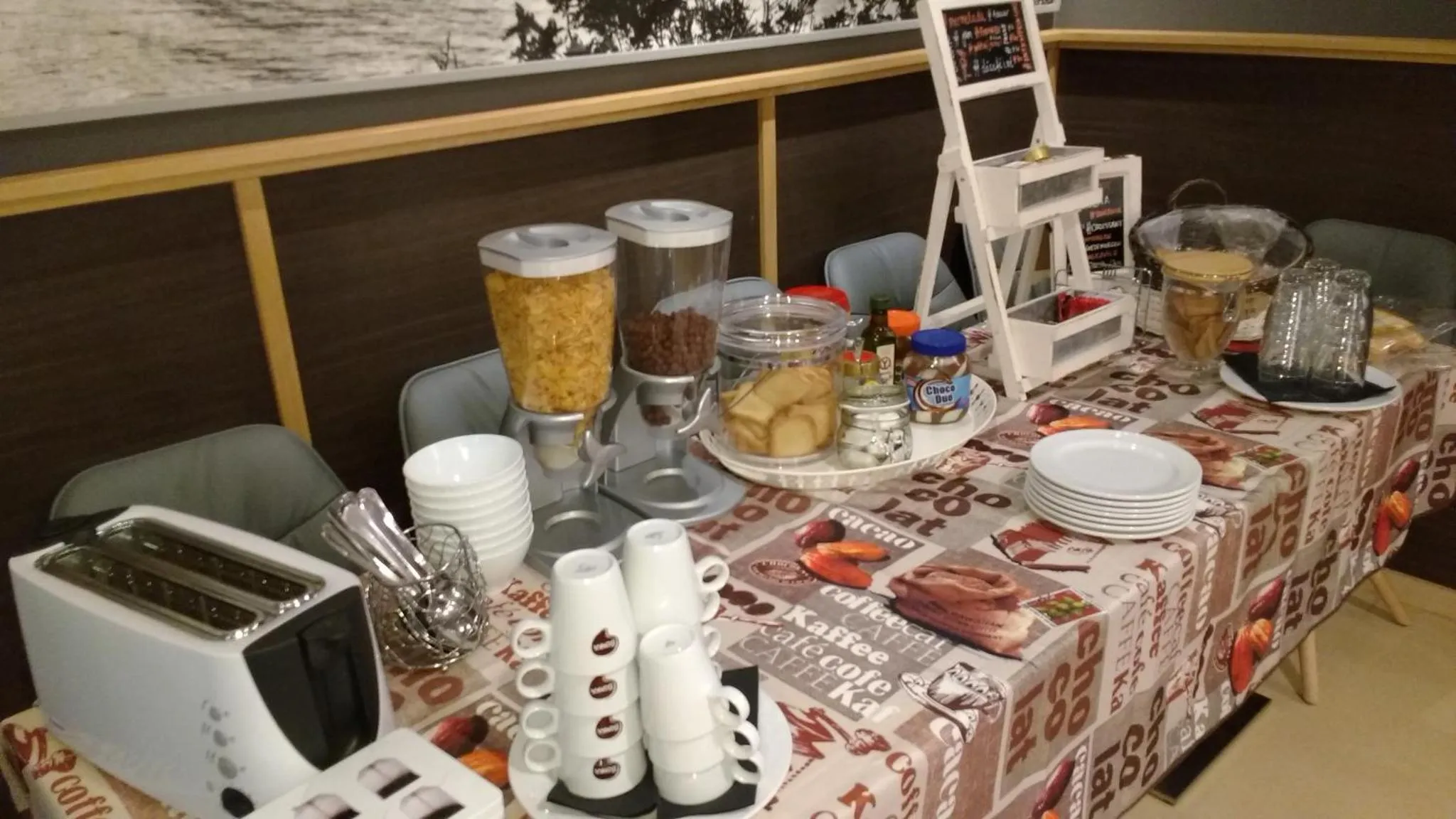 Un buffet propose des céréales, des pâtisseries et des boissons chaudes sur une table recouverte d'une nappe décorée.