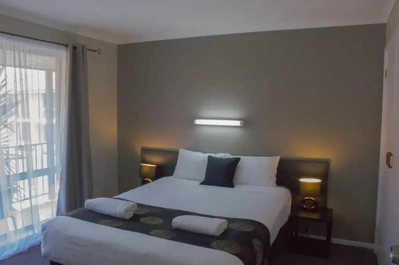 Une chambre avec un grand lit recouvert d'une courtepointe sombre et de coussins.