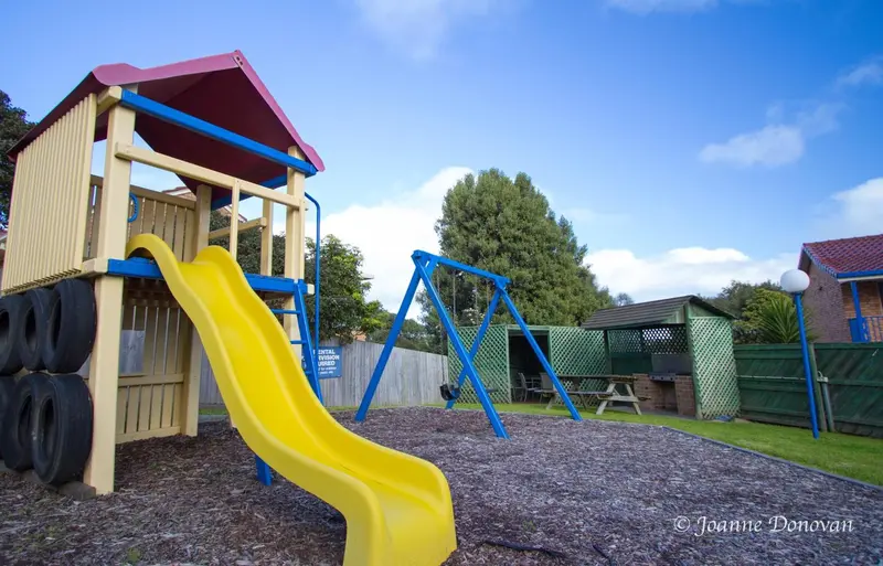Aire de jeux colorée avec toboggan et balançoires sur sol en copeaux de bois.