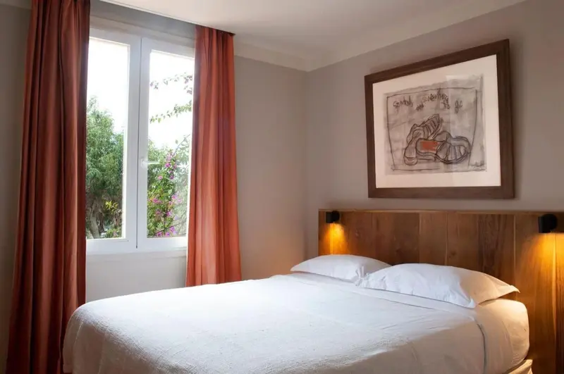 Une chambre lumineuse avec un lit blanc et un tableau au mur.