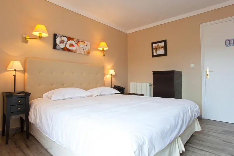 Une chambre lumineuse avec un grand lit recouvert d'une couette blanche.