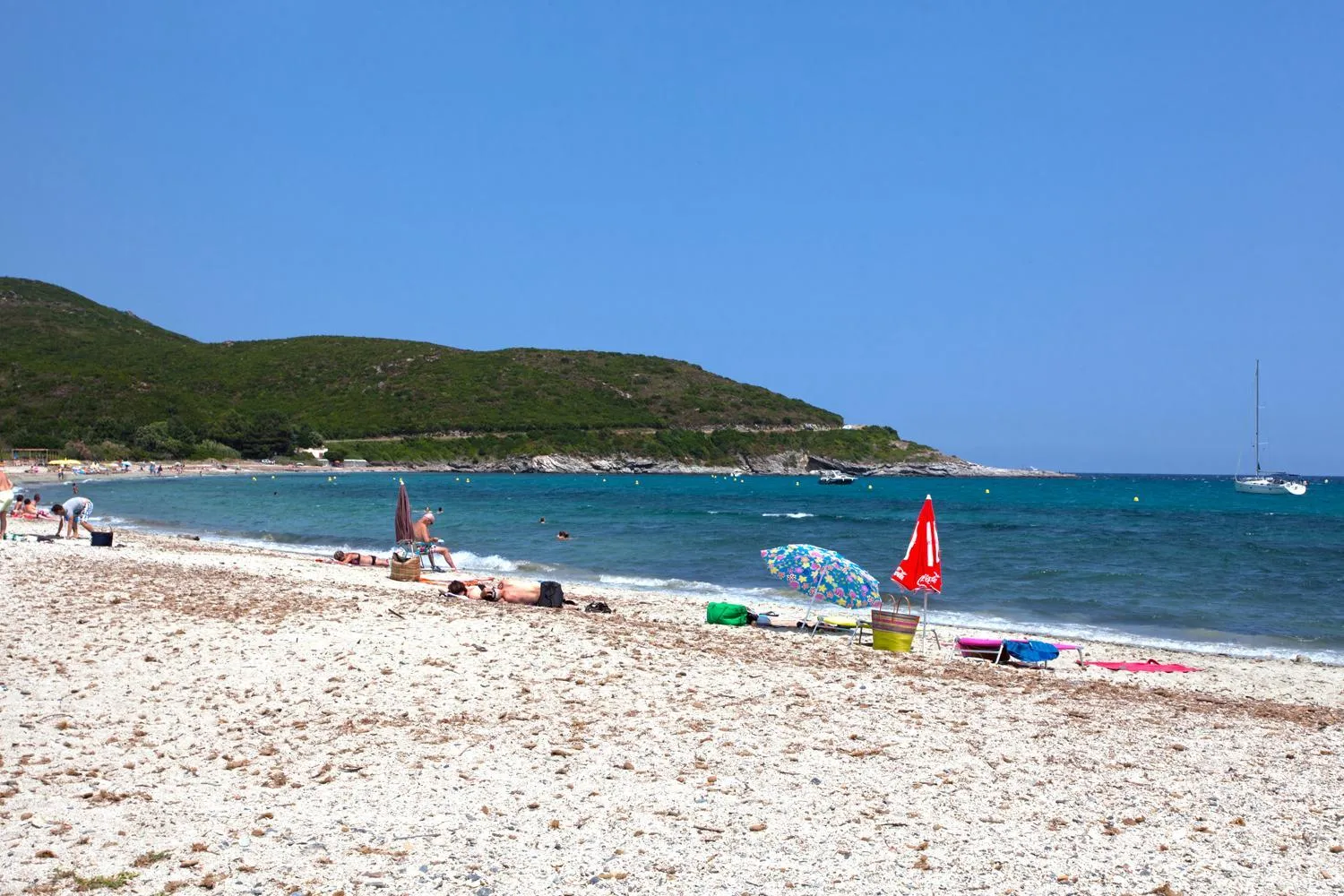 Une plage de sable clair avec des parasols colorés et des personnes se relaxant au soleil.