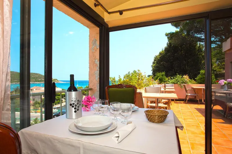 Une table dressée avec une bouteille de vin et de la vaisselle donne sur une vue dégagée sur la mer.