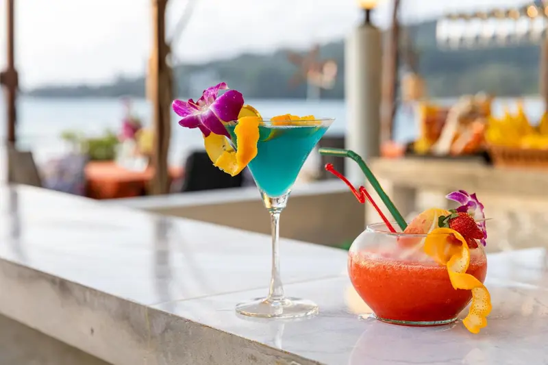 Des cocktails colorés sont présentés sur un comptoir blanc avec vue sur la mer.