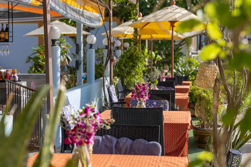 Terrasse ombragée avec tables et chaises colorées, décorée de plantes et de fleurs.