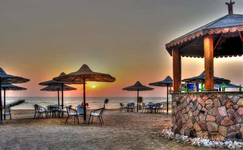 Terrasse de plage avec parasols et bar en pierre au coucher du soleil.
