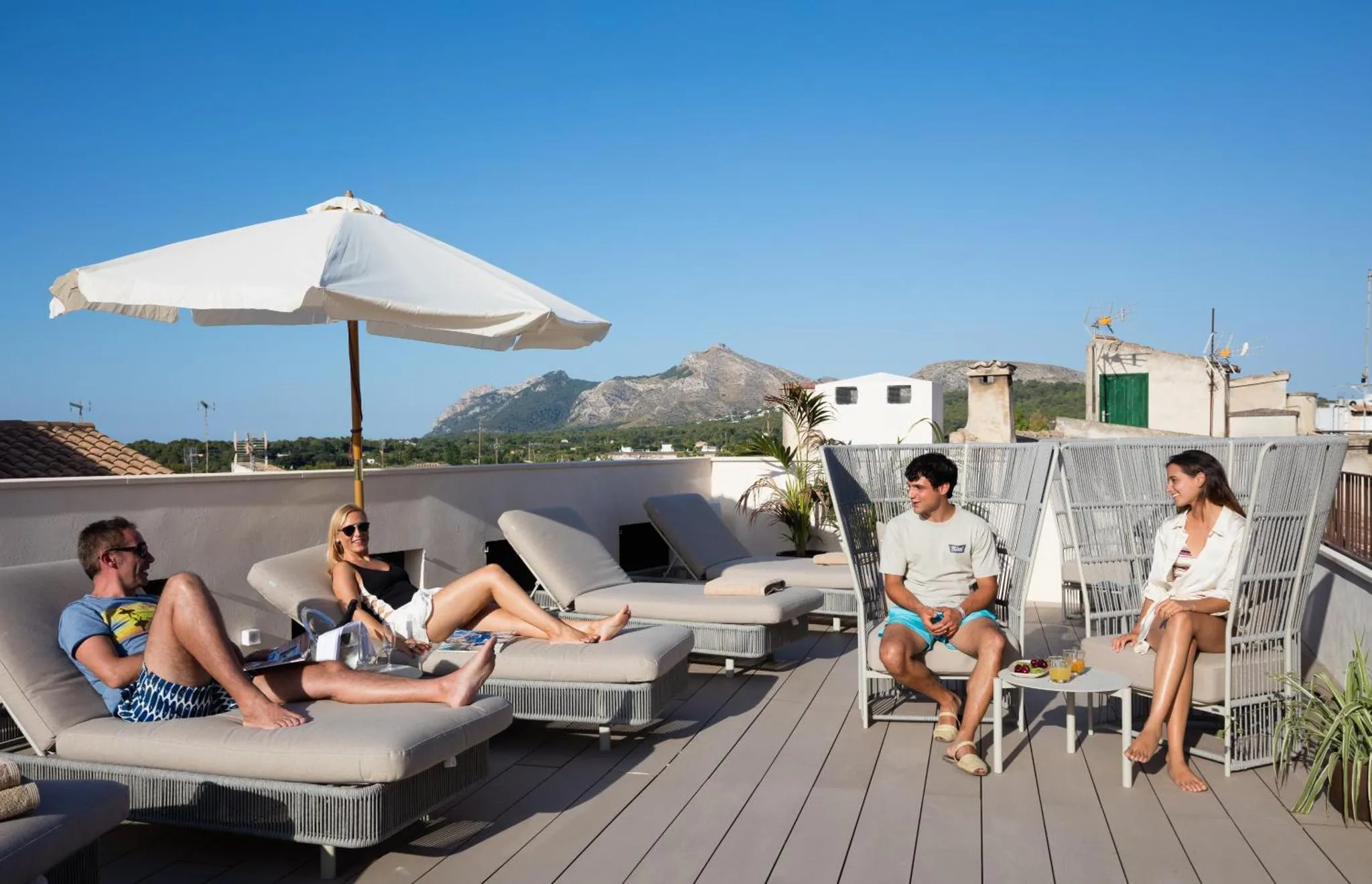 Des personnes se détendent sur une terrasse ensoleillée avec vue sur la mer et les montagnes.