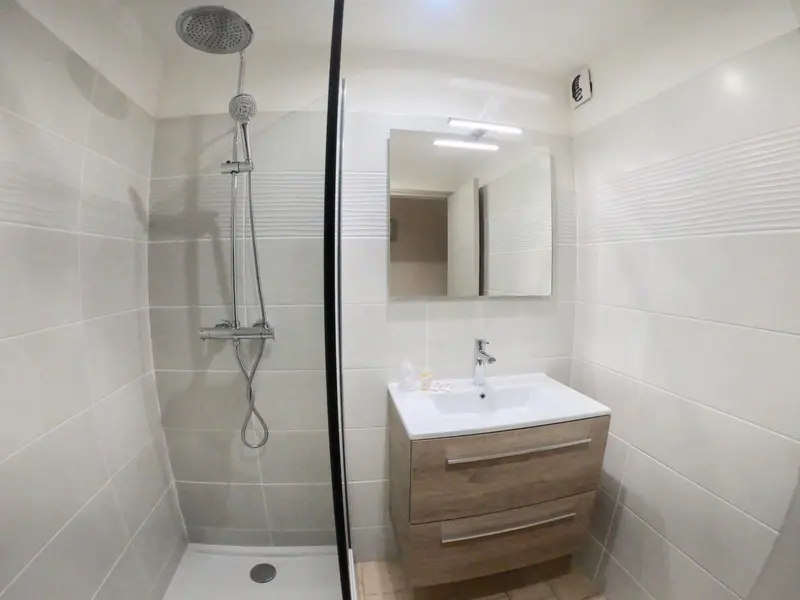Une douche à l'italienne avec un grand pommeau et un meuble vasque en bois clair.