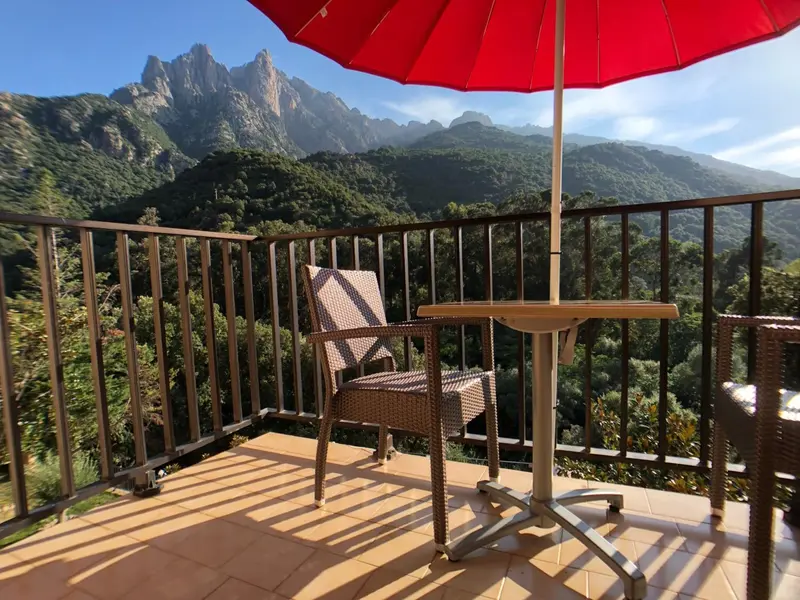 Une terrasse avec mobilier en osier offre une vue sur les montagnes verdoyantes.