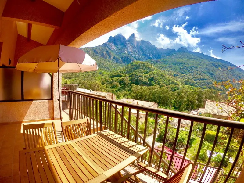 Terrasse ensoleillée avec mobilier en bois et vue sur les montagnes.