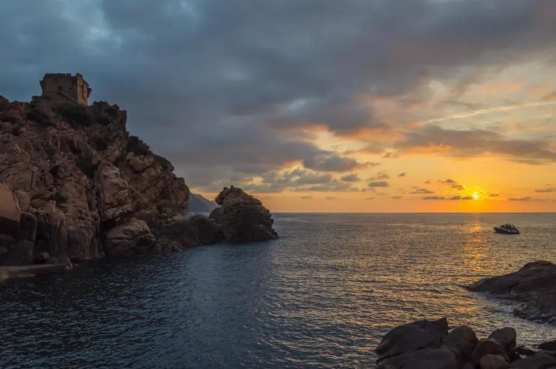 Coucher de soleil sur une côte rocheuse avec une mer calme.