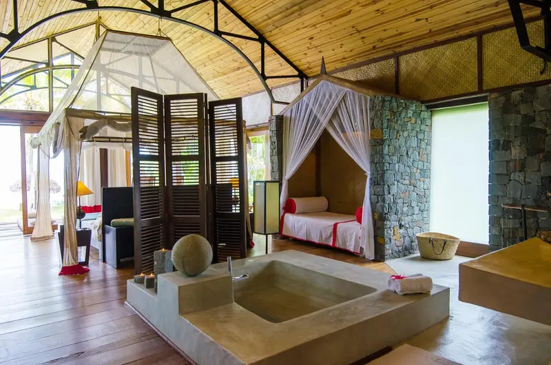 Une baignoire surélevée se trouve dans une chambre à coucher ouverte sur l'extérieur.