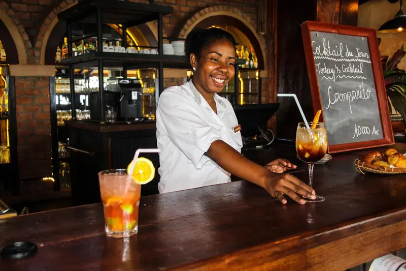 Une serveuse souriante derrière un comptoir de bar présente un cocktail.