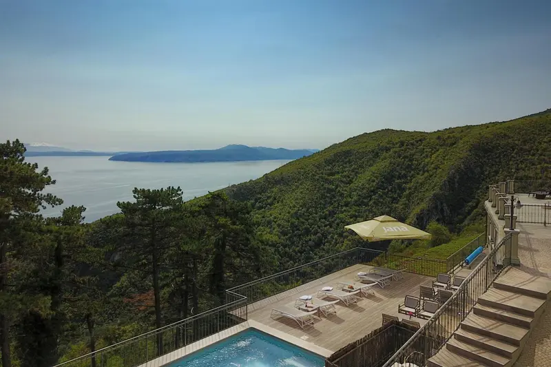 Terrasse avec transats et piscine surplombant la mer et les collines verdoyantes.