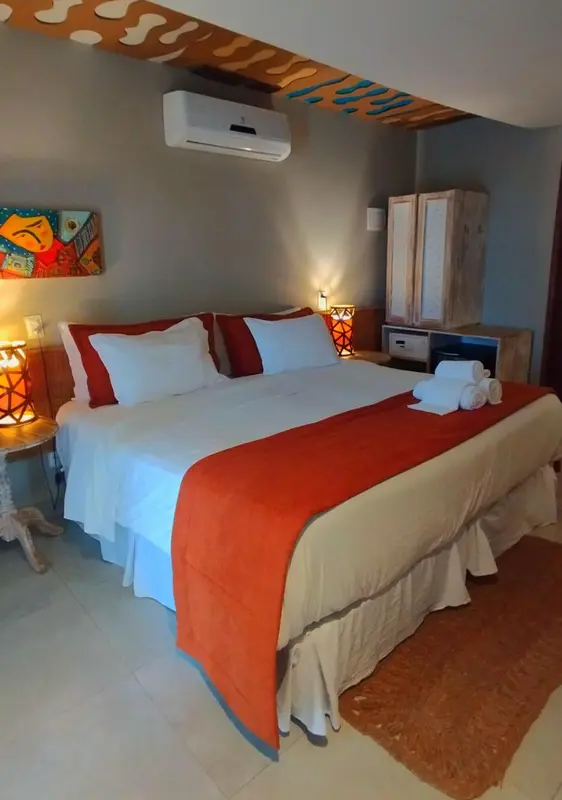 Une chambre lumineuse avec un grand lit recouvert d'une courtepointe orange et de coussins.