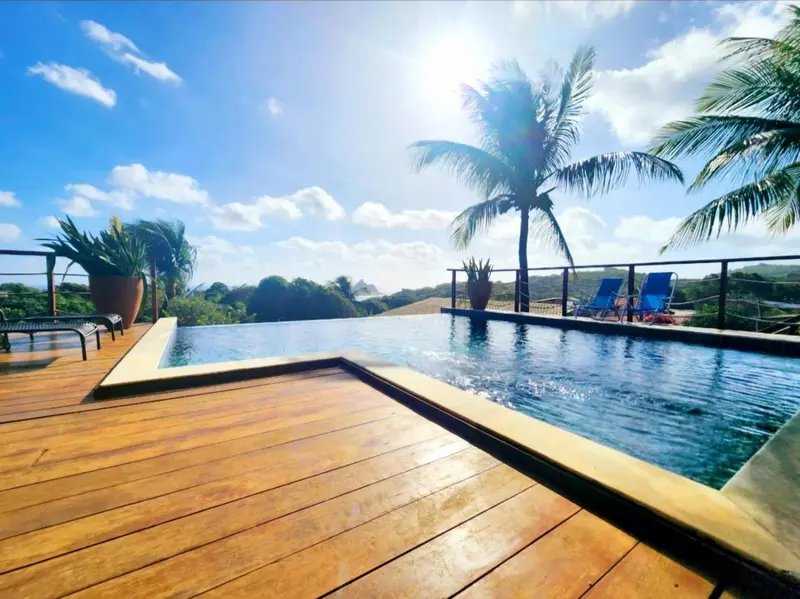 Une piscine à débordement avec une vue sur la végétation luxuriante et la mer.