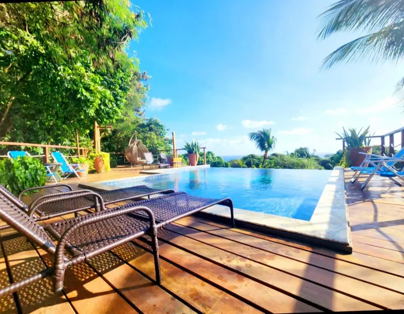 Transats et piscine à débordement avec vue sur la végétation luxuriante et la mer.