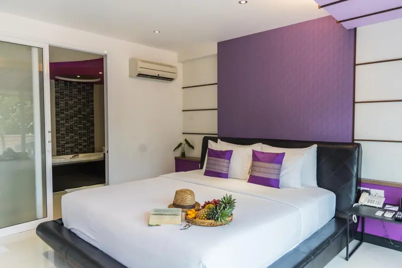 Une chambre lumineuse avec un grand lit recouvert de draps blancs et de coussins violets.