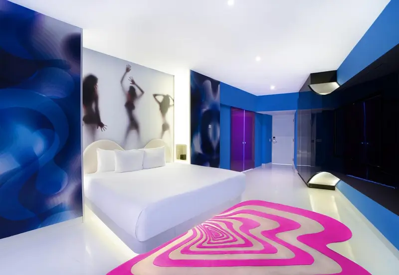 Chambre moderne avec un grand lit blanc et des motifs graphiques sur les murs et le sol.