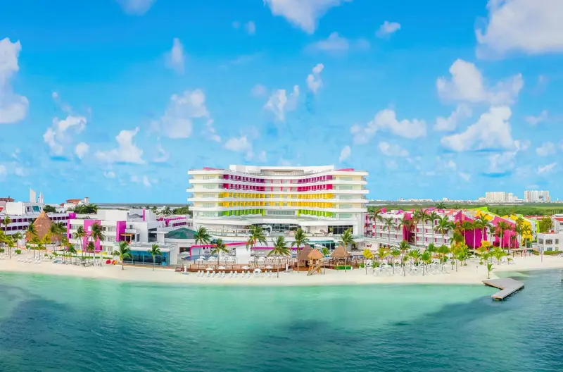 Vue aérienne d'un bâtiment coloré bordant une plage de sable blanc et une mer turquoise.